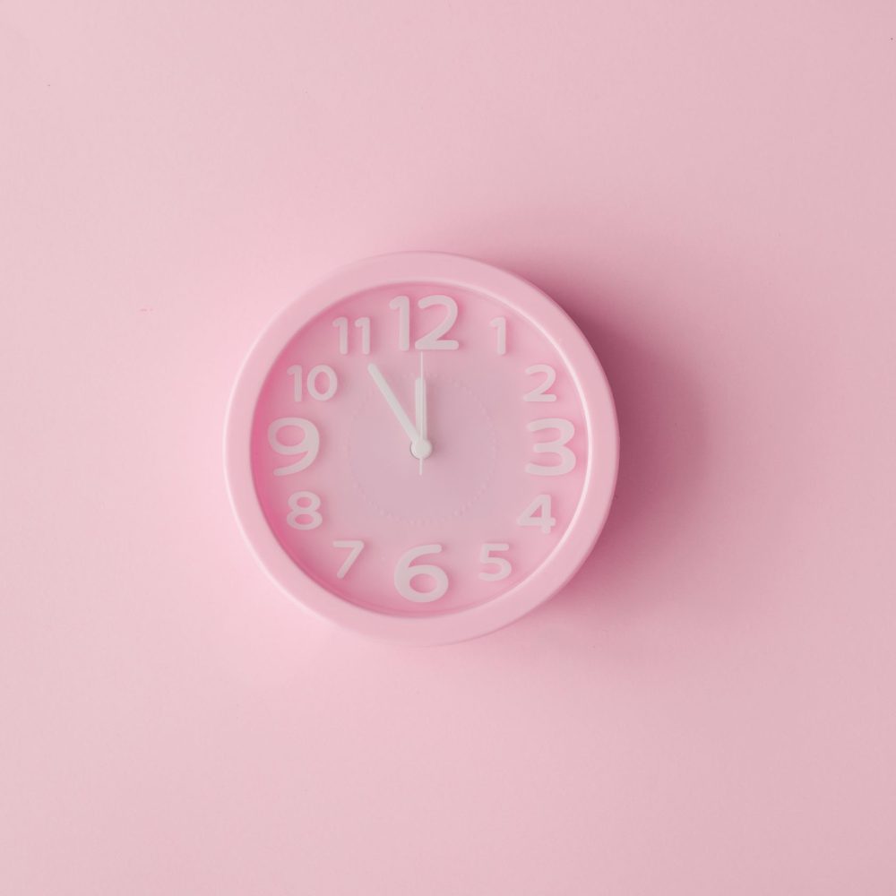 Pastel pink clock on pink painted wall. Minimal time concept. Chrismas eve or new year idea.